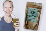 smiling woman with glass of green smoothie with straw beside a kratom powder in gold packaging