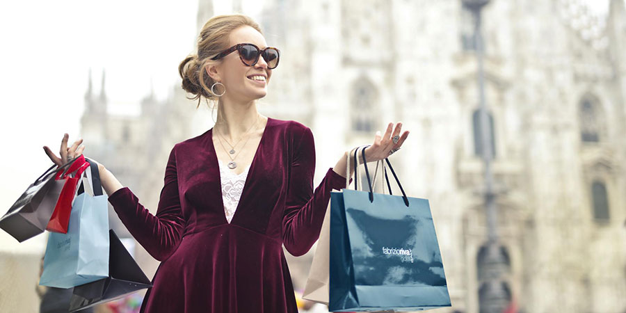 a woman wearing sunglasses and maroon velvet dress carrying several shopping bags